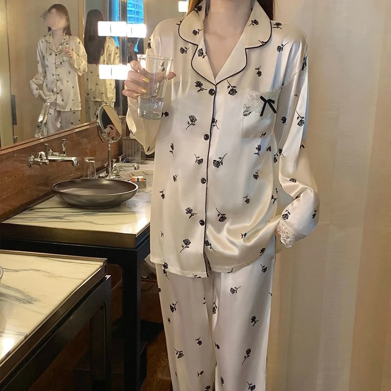 Cream satin long-sleeve pajama set with black rose print, black piping, lace cuffs, and bow-trimmed chest pocket